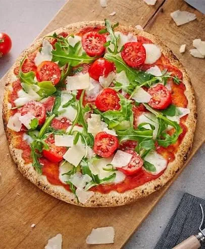 Pizza recién salida del horno con tomate, rúcula y láminas de queso, sobre una tabla de madera.