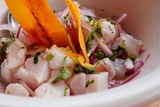 Ceviche peruano en un tazón blanco, con cebolla morada, culantro y camote asado.