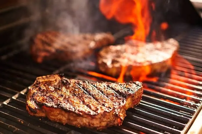 Cortes de carne marcados sobre la parrilla, con las llamas subiendo entre las rejillas.